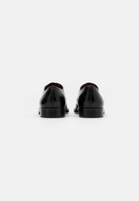 Scarpe in pelle verniciata nera con un design elegante, finitura liscia, punta arrotondata, tacco basso e rivestimento interno rosso a contrasto.
