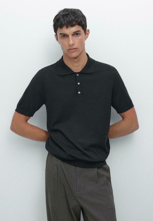Polo noir avec un col classique et trois boutons, associé à un pantalon rayé gris. Texture lisse, manches courtes et coupe décontractée.