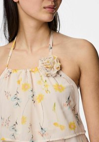 Ljus blommig halterneck-topp i beige, med gula och blå blommönster. Mjuk tyg med en tygblomma som accent på bysten.