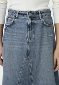 Denimkjol med hög midja, i ljusblå tvätt. Har framfickor, dragkedja och en centrerad slits fram för extra detalj.