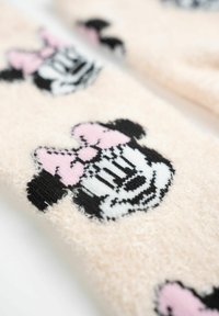 Calzini rosa pelosi con un motivo ripetuto di Minnie Mouse in bianco e nero, accompagnato da fiocchi rosa. Texture morbida e forma arrotondata.