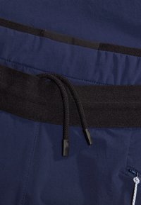 Mörkblå shorts med svart elastiskt midjeband. Har en dragsko med plastiga ändar och en sidoficka med dragkedja. Slät textur.