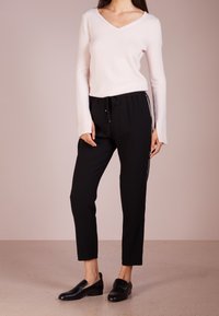 Lichtroze v-hals trui gecombineerd met zwarte tapered broek met zijstreep, met elastische tailleband en zwarte instapschoenen.