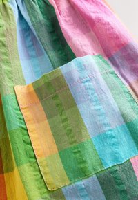 Tkanina w kratę o wielu kolorach, obejmująca odcienie zieleni, niebieskiego, różowego i żółtego. Tekstura jest miękka, z jedną kieszenią po lewej stronie.