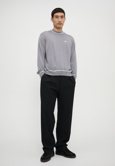 Maglione grigio a maglia con bordo bianco, caratterizzato da un piccolo logo sul petto. Abbinato a pantaloni neri larghi e sneakers nere.