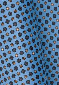 Niebieska tkanina z powtarzającym się wzorem małych ciemnozielonych kwadratów i pomarańczowych kwiatów, o teksturowanej powierzchni.