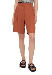 Roestkleurige high-waisted shorts met plooien, gemaakt van lichte stof. Gestyled met een gebloemd topje en zwarte sandaaltjes met bandjes.