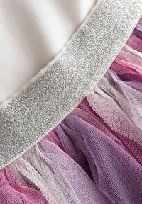 Tessuto bianco con banda argentata glitterata sopra strati arricciati di tulle in rete rosa, viola e lavanda.