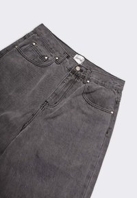 Jeans in denim nero con cinque tasche, accessori in metallo e vita media. Il tessuto ha un aspetto testurizzato e dettagli di cucitura minimi.