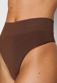 Smeđe donje rublje s visokim strukom napravljeno od mekog materijala, s glatkim pojasom na kojem je utisnuto "organic basics". Minimalistički dizajn, bez vidljivih šavova.