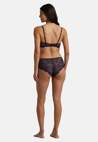 Marinblå spetsbehå och matchande trosor, med scallopade kanter, justerbara axelband och blommönstrad spets. Bakvy visas.