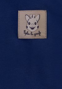 Tessuto blu navy con un'etichetta beige cucita sopra che raffigura un personaggio di giraffa sorridente con accenti neri e il testo "Sophie la girafe."