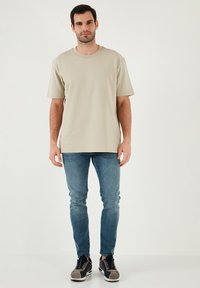 Beige tričko s krátkým rukávem a kulatým výstřihem, v kombinaci se světle modrými slim-fit džíny a šedými a černými teniskami. Jednoduchý design a pohodlný střih.