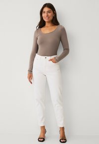 Hnědý dlouhý rukáv body spojený s bílými džíny s vysokým pasem. Džíny mají zapínání na knoflík a rovný střih, doplněné černými podpatky.