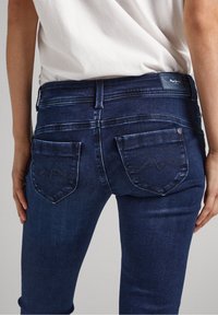 Mörkblå denimjeans med slim fit, som har två bakfickor med en böjd sömdetalj och en märkeselastisk midja bak.