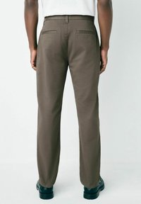 Pantaloni maro cu un design drept, având buzunare la spate și o textură a materialului neted, asortați cu pantofi negri.