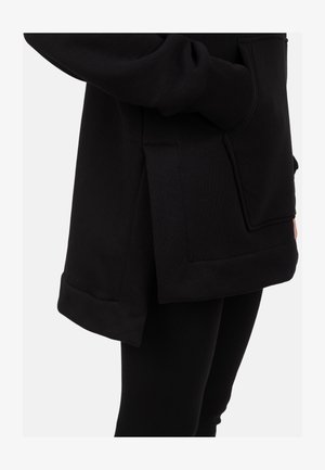 Fekete kapucnis pulóver elején zsebbel, oldalsó sliccel és laza szabással. Az anyag sima tapintású, bordázott részletekkel kiegészítve.