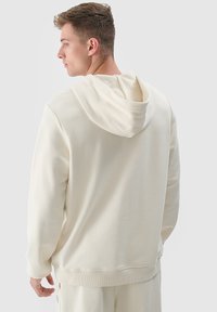 Crème-kleurige hoodie met een trekkoordcapuchon, ribgebreide manchetten en een losse pasvorm. Voorzien van een soepele textuur en een minimalistisch ontwerp.