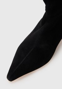 Stivale alla caviglia in suede nero con punta affilata e texture liscia. Lo stivale presenta una silhouette adatta e dettagli di cucitura discreti lungo la cucitura.