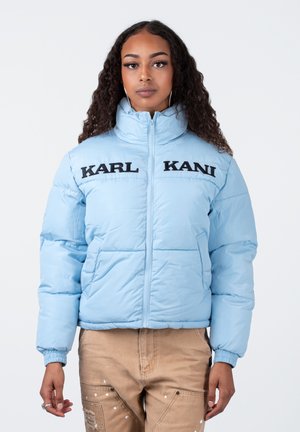 Lyseblå polstret jakke med sort "KARL KANI" branding. Har høj krave og elastiske manchetter, parret med beige bukser.