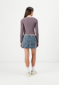 Violetinės raukšlėtos ilgomis rankovėmis palaidinės ir mėlynos džinsinės sijono, turinčio prigludusi�ą struktūrą, nebaigtą apipjaustymą ir dvi galines kišenes. Baltos sportinės bateliai su tekstūruotais padais.