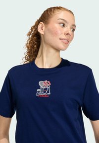 Námornícky modré bavlnené tričko s bielym a červeným vyšívaným dizajnom kvetináča, tenisovej rakety a tašiek na oblasti hrudi.