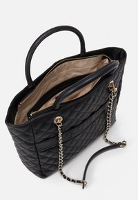 Sort quilted tote bag med dobbelthåndtag, guld accenter og en kædestrop. Beige indvendig med flere rum og lynlåslukninger.