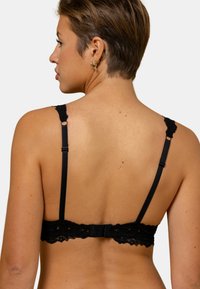 Bralette en dentelle noire avec des bretelles réglables, une bordure festonnée et une fermeture à crochets au dos, mettant en valeur un motif texturé.