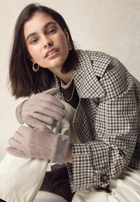 Beige ruskindshandsker med blødt gråt fleecekant og syede detaljer. Modellen har en ternet frakke på over en hvid top og lyse bukser.