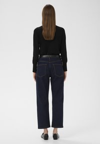 Sötétkék farmernadr�ág egyenes szárú kivitelben, látható varrással, két hátsó zsebbel és fekete övvel. Hosszú ujjú fekete felsővel viselve.