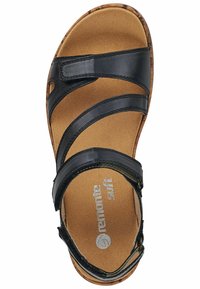Sandalia de cuero negro con tres correas superiores, una plantilla acolchada en tono marrón y una suela tipo corcho. Presenta la marca "remonte soft".