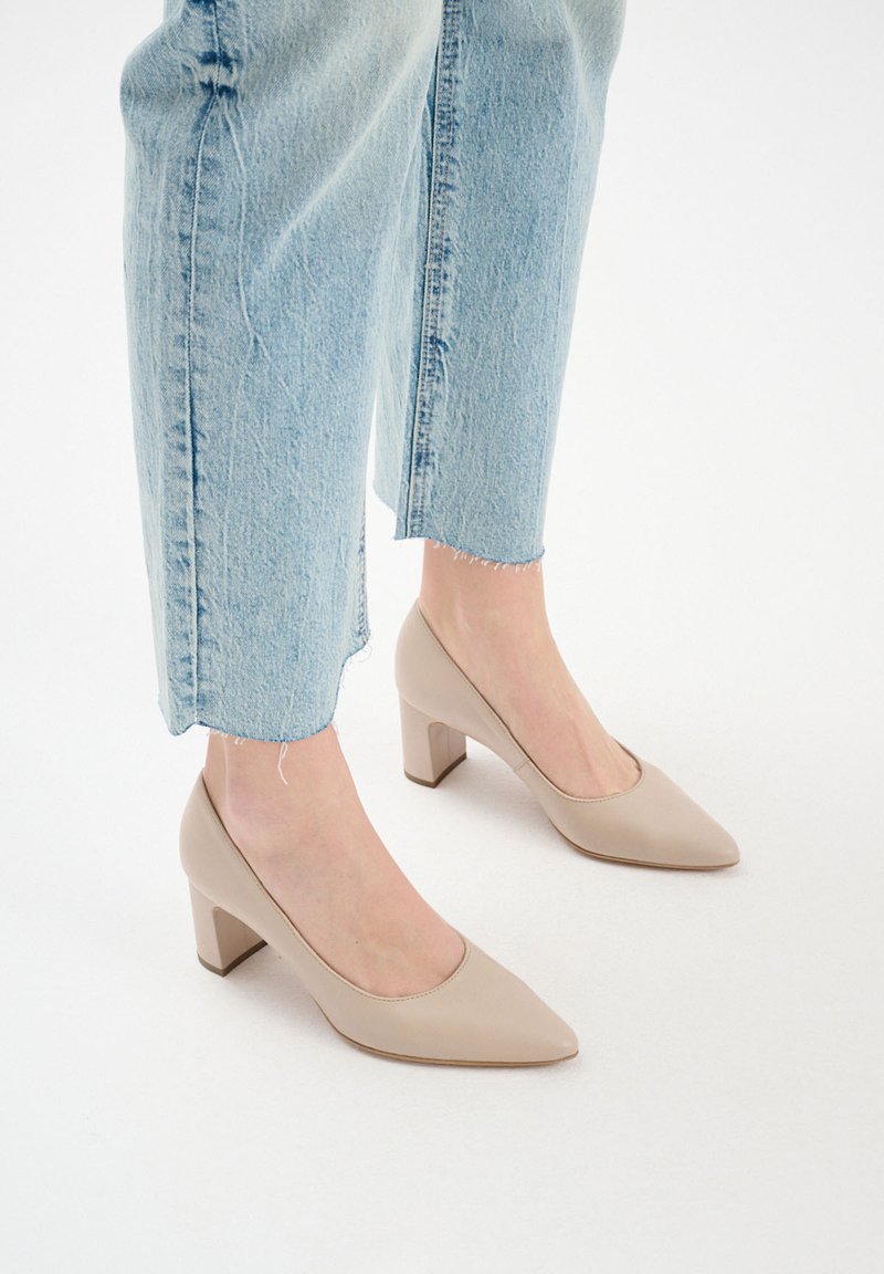 Beżowe skórzane czółenka z ostrym noskiem i słupkowym obcasem. Noszone z jasnoniebieskimi dżinsami z postrzepionymi nogawkami, co podkreśla swobodny styl.