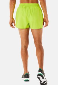 Pantalones cortos atléticos en verde neón con una cinturilla elástica, textura suave y un ajuste relajado, combinados con zapatillas de correr negras que tienen acentos en verde.