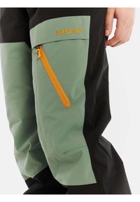 Pantaloni impermeabili neri e verdi con una tasca con zip arancione, caratterizzati da un design elegante e tessuto liscio e resistente. Dettaglio con logo ricamato.