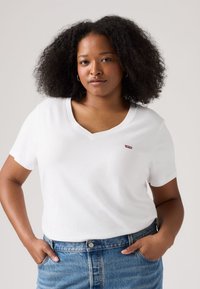 Balta kokvilnas T-krekls ar V veida izgriezumu un īsām piedurknēm, kreisajā krūtīs neliels sarkans Levi's logotips. Kombinēts ar džinsa šortiem.