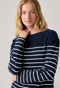 Meriino paita tummansinisenä, valkoisilla vaakaraitoja, pitkät hihat ja leveä kaula-aukko. Pehmeä rakenne ja vaivaton kaarroke.