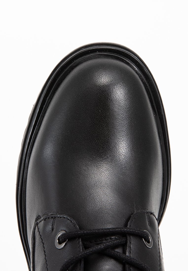 Gros plan sur une chaussure noire en cuir à lacets avec un bout arrondi et une semelle épaisse sur fond blanc.