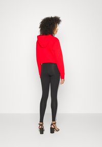 Rode cropped hoodie met een capuchon, gecombineerd met zwarte hoog-waist leggings met witte zijstrepen. Model draagt zwarte hakken.