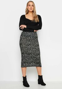 Mustapintainen ribattu pitkähihaine neuletakki yhdistettynä mustaan kynähameeseen, jossa on valko-harmaa abstrakti kuvio. Mallilla on päällään mustat nilkkurit.