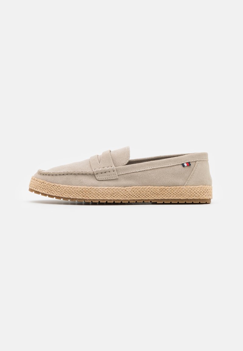 Beige Wildleder-Slipper mit strukturierter Jutensohle und einem dezenten Akzentstreifen. Runde Zehenpartie und gestickte Details entlang des Obermaterials.