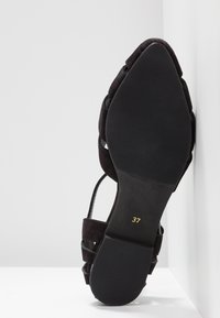 Sandale plate en suede noir avec une semelle en caoutchouc texturé, design ouvert et sangle réglable, taille marquée 37 en or.