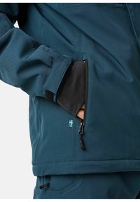 Wasserabweisende türkise Jacke mit einer Reißverschlusstasche, verstellbaren Manschetten und einem kleinen schwedischen Flaggenakzent. Glatte Textur und modernes Design.