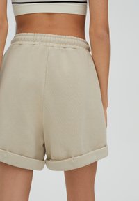 Shorts en coton beige avec taille élastique et poignets retroussés. Le tissu semble doux avec une texture lisse, arborant un design simple.