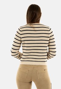 Maglione a righe color crema con righe orizzontali blu navy, tessuto strutturato, colletto rotondo e polsini a coste, abbinato a pantaloni beige.