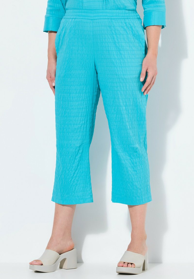 Pantalons turquoise raccourcis avec un design texturé et matelassé. Assortis à des sandales à plateforme de couleur claire.