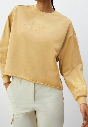 Světle béžová mikina s cropped designem, na přední straně a levém rukávu s embosovaným nápisem "MALIBU CALIFORNIA". Měkká textilie.