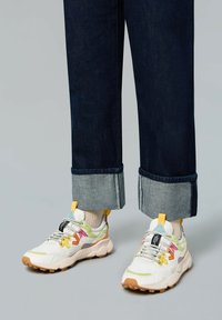 Zapatillas con acentos multicolores, con un upper blanco y gris claro, suela de goma texturizada y cordones visibles. Jeans de mezclilla con los puños enrollados.