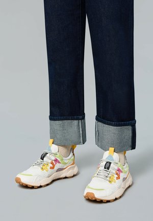 Sneakers with multicolored accents, featuring a white and light gray upper, textured rubber sole, and visible lacing. Denim jeans with rolled cuffs.