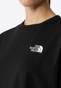 Melna kokvilnas T-kreklu ar apaļu kakla izgriezumu un īsām piedurknēm, ar balto izšūto "The North Face" logo uz krūšu.