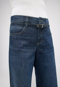 Dunkelblaue Denim-Jeans verfügen über fünf Taschen, einen klassischen Bund und eine silberne Schnalle mit Gürtelschlaufen. Glatte Textur und gerades Bein-Design.